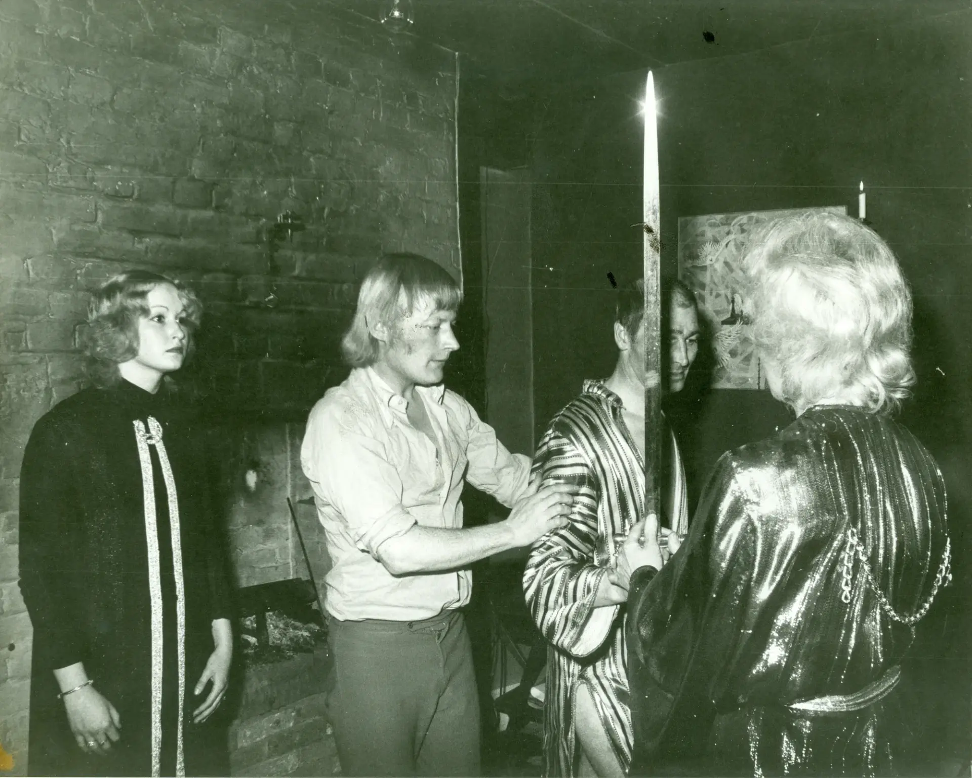A candlelit rite in a brick-walled room: robed figures gathered around a raised sword.